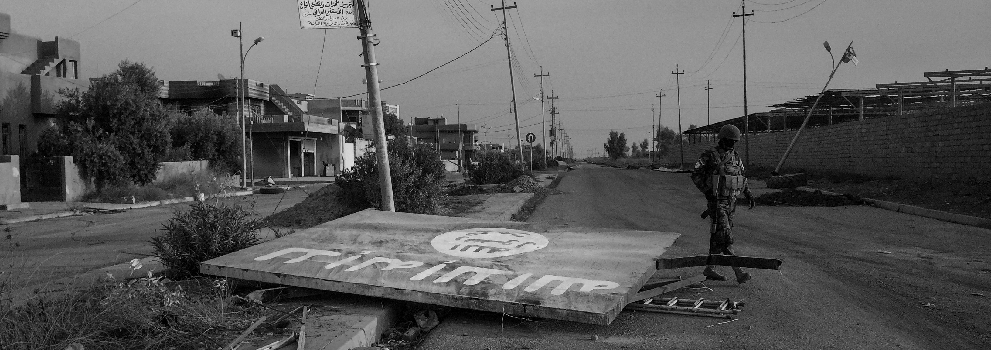 An Assyrian soldier from the Nineveh Protection Unit walks past a destroyed ISIS sign in the middle of the road on Nov. 8, 2016, in Qaraqosh, Iraq.