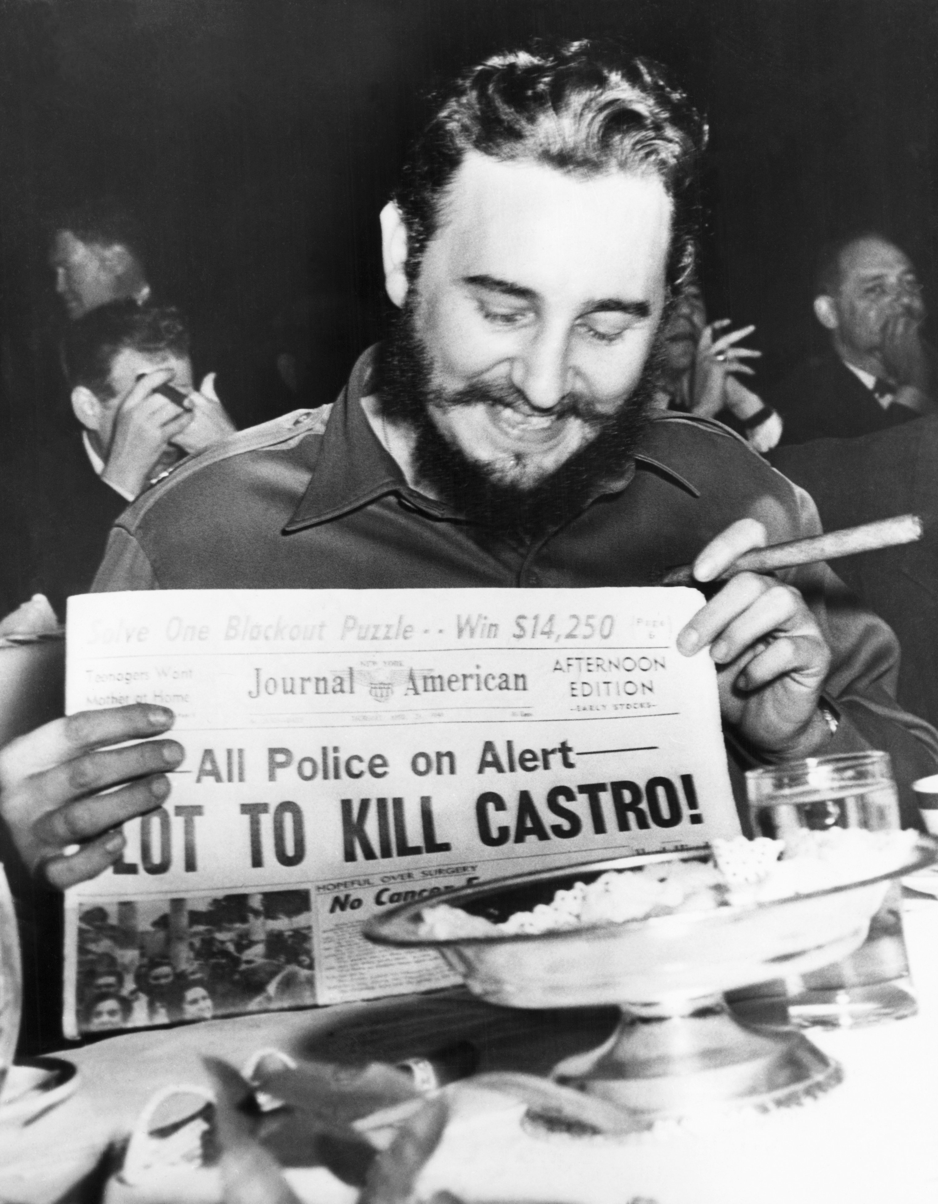 Seeming quite amused, Castro holds up a newspaper headlining the discovery of a plot to kill him in New York City on April 23, 1959.&nbsp;