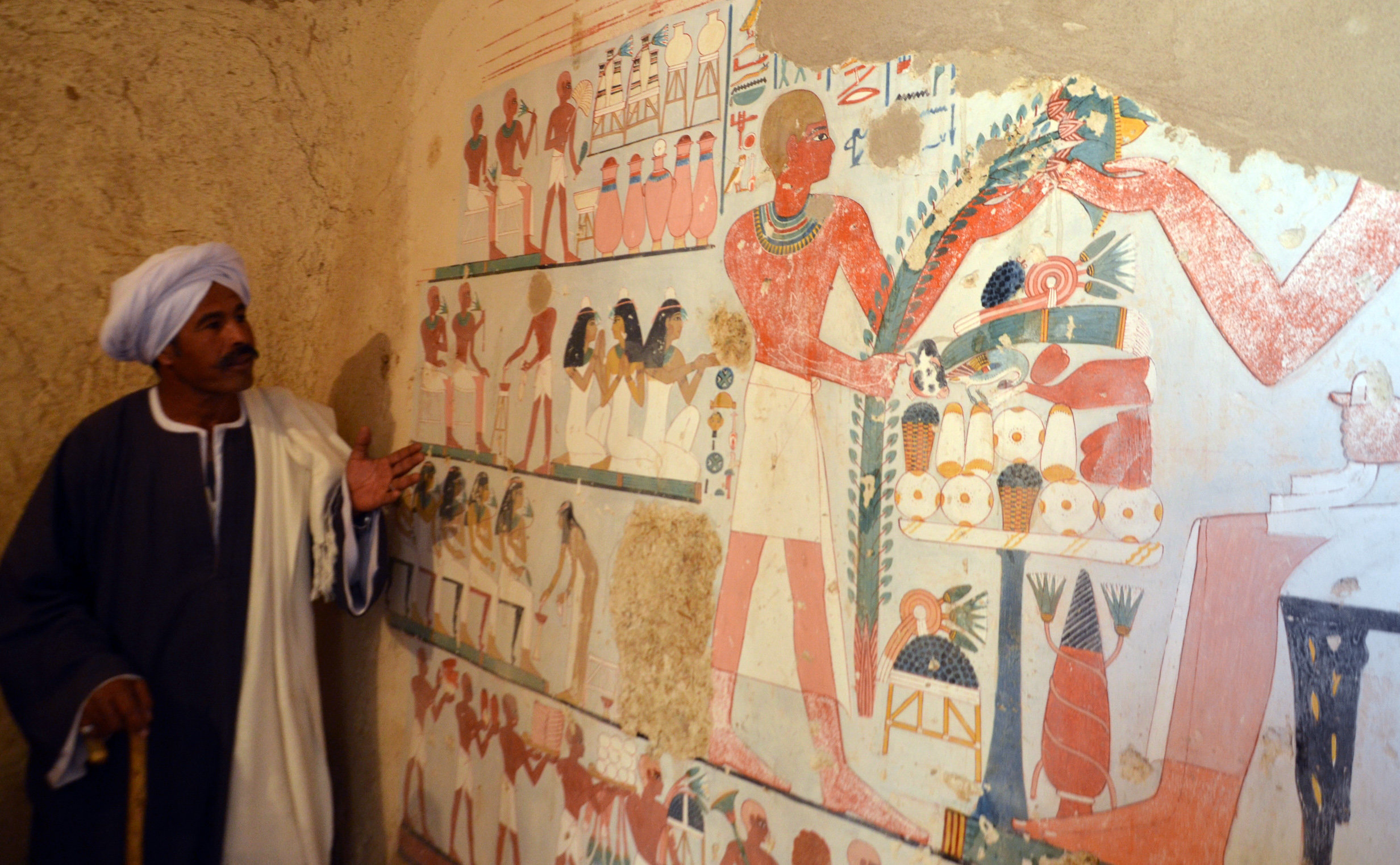 <strong>'It looks like it was painted yesterday' - An&nbsp;worker stands next to an ancient Egyptian mural found in one of the newly explored tombs&nbsp;</strong>