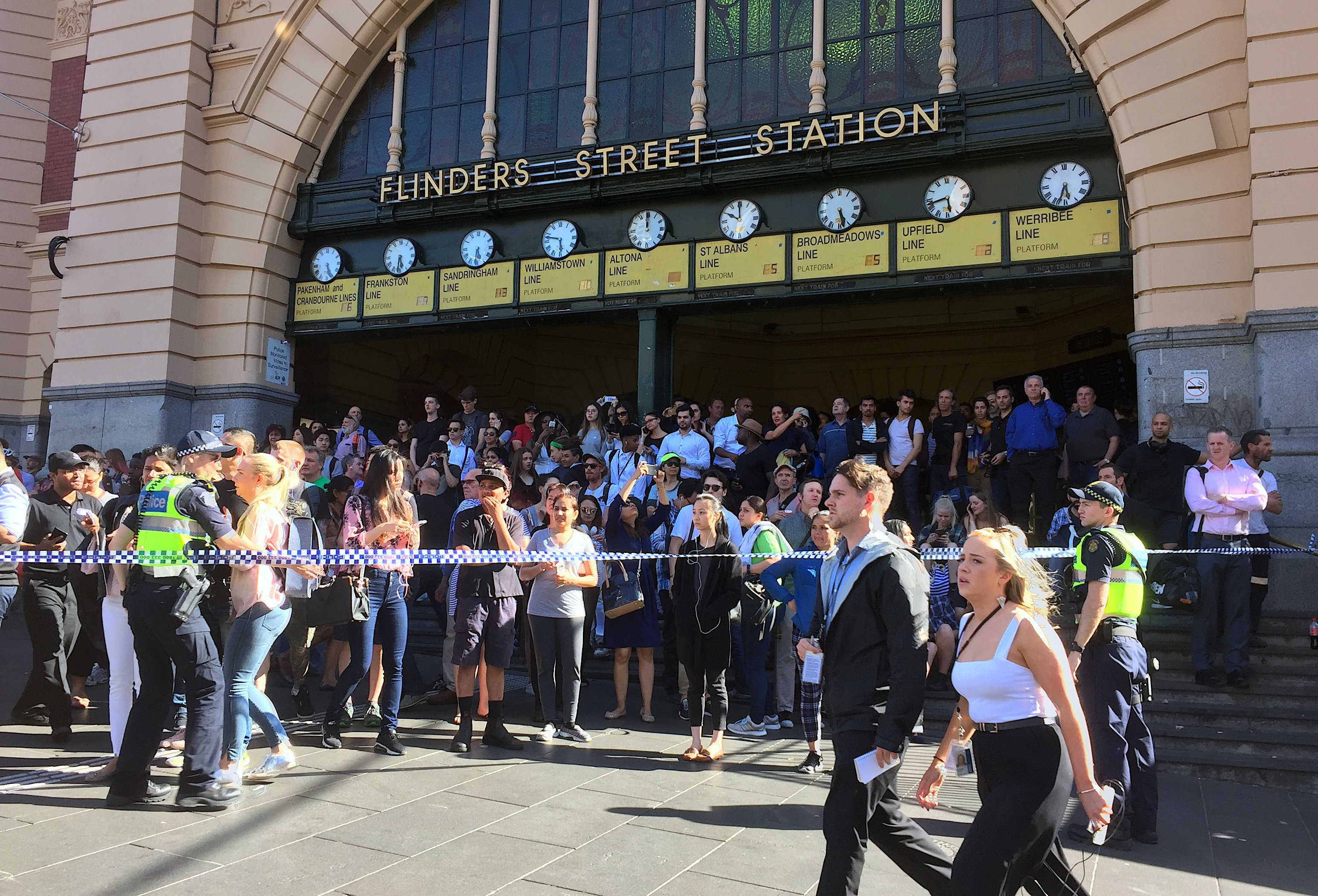 <strong>Members of the public stand behind police tape after a car ploughed into pedestrians at a crowded intersection near the Flinders Street train station in central Melbourne, Australia.</strong>