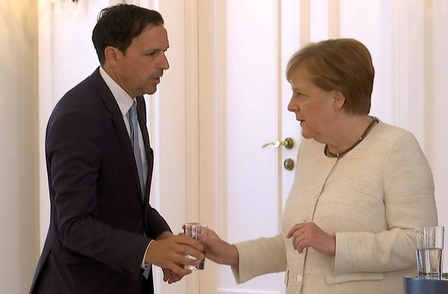 Angela Merkel recibe un vaso de agua, tras sufrir nuevos temblores durante un acto oficial.