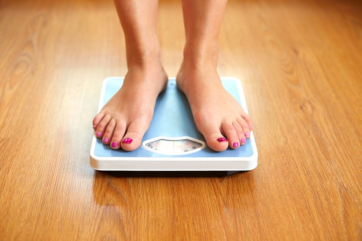 Female bare feet with weight scale on wooden floor