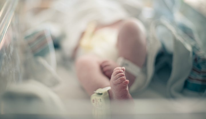 Newborn baby lies on its back surrounded by blankets in hospital bassinet with only its feet and ankle tracking bracelet in focus, photographed with shallow depth of field allowing for ad space.