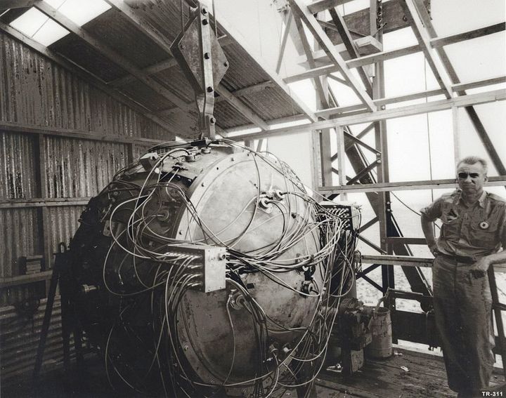 Norris Bradbury, group leader for bomb assembly, stands next to the partially assembled Gadget.