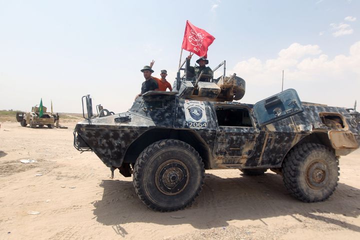 Iraqi Shiite fighters from the Popular Mobilisation units, supporting the Iraqi government forces, flash the sign of victory on an armoured vehicle as they guard a position on July 15, 2015 on the northern outskirts of the city of Fallujah, west of the capital Baghdad, during an offensive to retake the Anbar capital, Ramadi. Iraqi security forces, Shiite paramilitaries and Sunni tribal fighters advanced towards Ramadi and Fallujah, the two main cities in the western province of Anbar in their latest push to recapture the capital from Islamic State (IS) group's jihadists. At center is the flag of Al-Hashd al-Shaabi, a Popular Mobilisation unit led by Shiite cleric Moqtada al-Sadr. AFP PHOTO / AHMAD AL-RUBAYE (Photo credit should read AHMAD AL-RUBAYE/AFP/Getty Images)