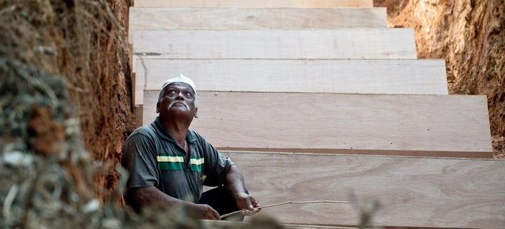 A Malaysian Muslim man sits amid coffins in a pit during the re-burial of remains believed to be those of ethnic Rohingya found at human-trafficking camps in the country's north, at Kampung Tualang some 16kms east of Alor Setar on June 22, 2015. Malaysian authorities on June 22 held a sombre mass funeral for 21 suspected ethnic Rohingya found in human-trafficking graves last month, with fellow Muslims praying for the unidentified victims to find a place in heaven. AFP PHOTO / MANAN VATSYAYANA (Photo credit should read MANAN VATSYAYANA/AFP/Getty Images)