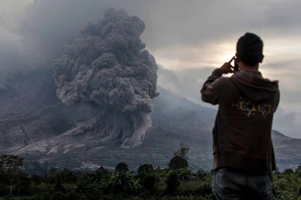 KARO, NORTH SUMATRA, INDONESIA - JUNE 20: A man take a picture as Mount Sinabung spews pyroclastic smoke, seen from Tiga Kicat village on June 20, 2015 in Karo District, North Sumatra, Indonesia. According to The National Disaster Mitigation Agency, more than 10,000 villagers have fled their homes since the authorities raised the alert status of Mount Sinabung erupting to the highest level. (Photo by Ulet Ifansasti/Getty Images)