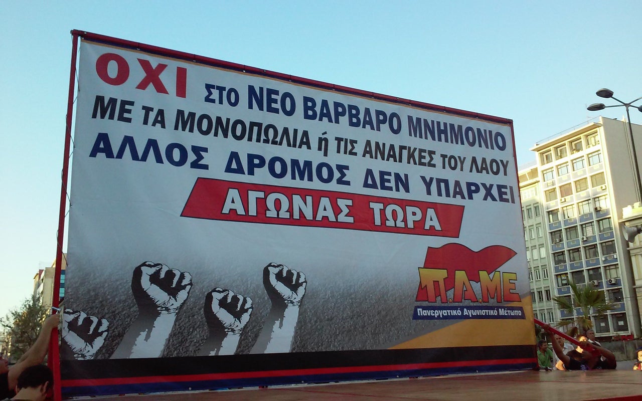 A protest banner reads "NO to the new barbaric memorandum. Either with the monopolies or with the needs of the people. There is no other way. FIGHT NOW. PAME."