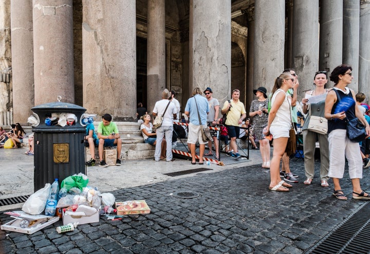 Tourists stand next to a bin overflowing with waste in front of the Ancient Pantheon, in central Rome on July 27, 2015.