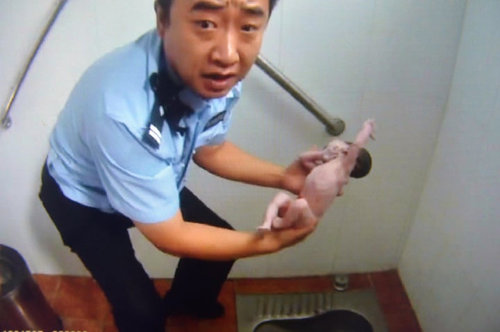 This frame grab of a police video taken on Aug. 2, 2015, shows a policeman holding an abandoned newborn baby in a public toil
