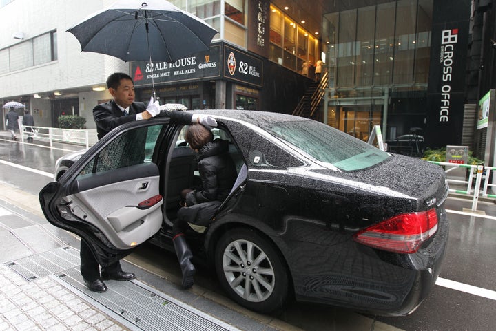 A driver opens the door for a customer during a demonstration outside the Uber Japan Co. office in Tokyo, Japan, on Wednesday, March 5, 2014.