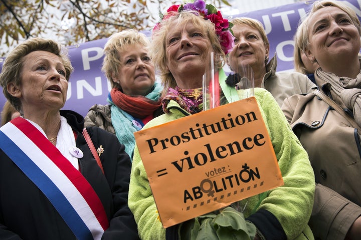 <p>Former French sex worker Rosen Hicher (center), an activist for the abolition of prostitution, holds a placard at a Paris demonstration in 2014, calling for criminal penalties for clients of sex workers.</p>
