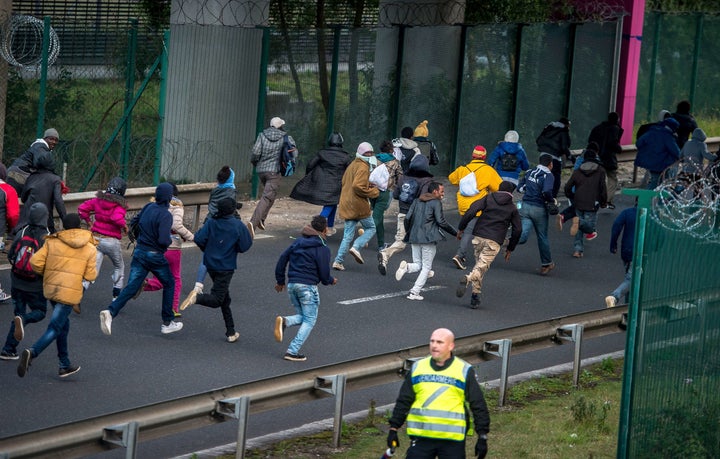 Migrants trying to reach the Channel Tunnel run past a policeman on the Eurotunnel site in Coquelles near Calais, northern France, on late July 29, 2015. 