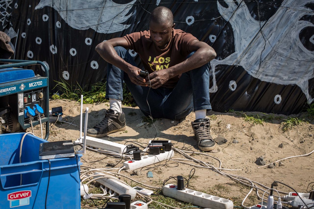 A man uses a generator to charge a mobile phone in a makeshift camp near the port of Calais, France, on Aug. 1, 2015.