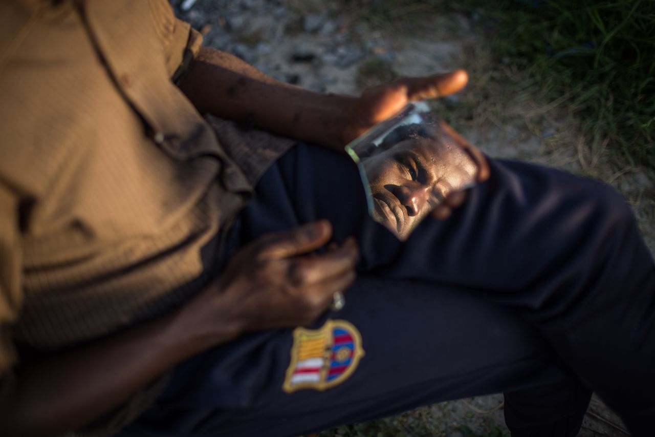 A Sudanese man is seen in a piece of broken mirror whilst having his hair cut in a makeshift camp near the port of Calais on Aug. 2, 2015. 