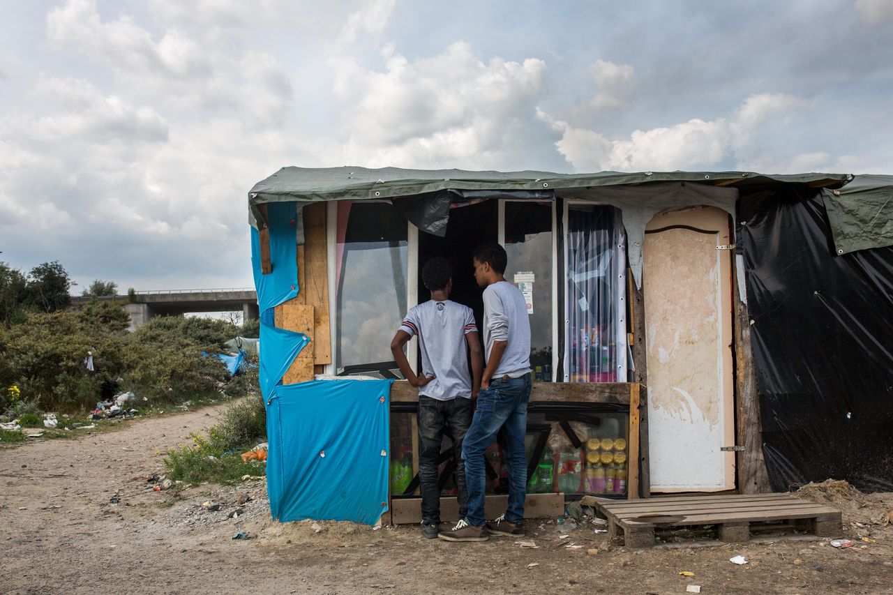 Men buy from a shop run by Afghanis at a makeshift camp near the port of Calais on July 31, 2015. 
