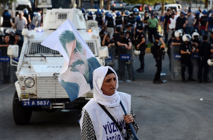 A woman holds a flag of jailed Kurdish leader Abdullah Ocalan as she stands opposite Turkish riot police in Diyarbakir on August 1, 2015. 