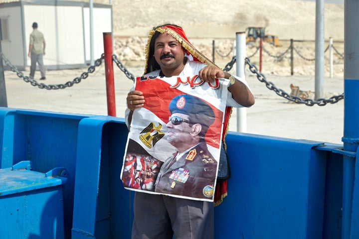 A man wears an Egyptian flag and holds a poster of Egyptian President Abdel Fattah al-Sisi beside a section of the New Suez Canal in Ismailia, Egypt, on Aug. 5, 2015.