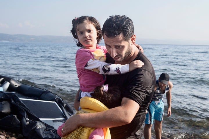 A Syrian father holds his two daughters after their boat lands on Aug. 2, 2015 near Molyvos, on the island of Lesvos, Greece.