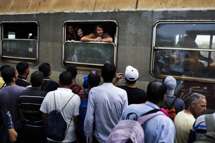 Passengers of the Belgrade-Thessaloniki international train watch migrants waiting to reach a train heading to the Serbian border in Gevgelija, on the Macedonian-Greek border, on Aug. 7, 2015.