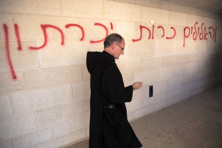 A priest walks past a graffiti reading in Hebrew 'idols will be cast out' as he inspects the damage at the Church of the Multiplication at Tabgha, on the shores on the Sea of Galilee in northern Israel, on June 18, 2015, in the aftermath of a suspected arson attack