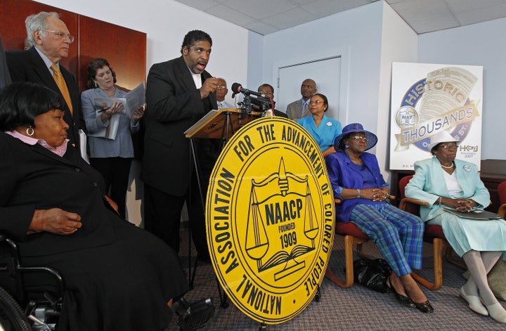 The Rev. William Barber, head of the N.C. NAACP, at podium, announces that the group is filing a lawsuit against the recently passed Voter ID bill during a press conference held in Durham, North Carolina, Tuesday, August 13, 2013. held in Durham, NC on August 13, 2013. Seated are plaintiffs Carolyn Q. Coleman, left, Mary Perry, second from right, and Rosanell Eaton, right. 