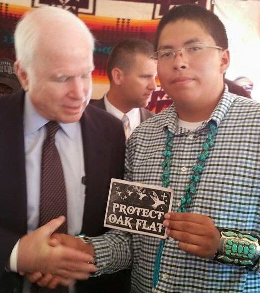 Navajo teen Adriano Tsinigine shakes the hand of Sen. John McCain while holding a small card protesting the sale of Native holy land to mining interests.