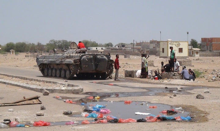 Yemenis sit near a tank used by members of the southern separatist movement parked in a deserted street in the port city of Aden's Dar Saad suburb, on April 14, 2015.