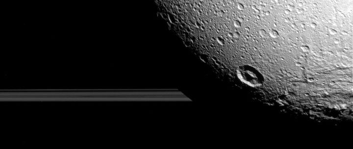 One of the newly released images of Dione, a moon of Saturn, showing the rings of Saturn behind it. The new images were taken earlier this month by the Cassini spacecraft.