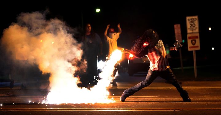 Edward Crawford throws back a tear gas container after tactical officers worked to break up a group of bystanders on Aug. 13, 2014.