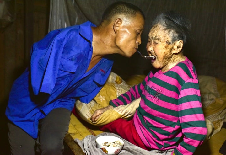 Chen Xingyin holds a spoon in his mouth to feed his mother.