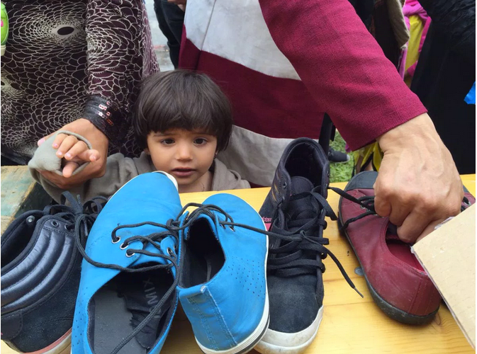 A Syrian girl looks at shoes as the older women grab a pair.
