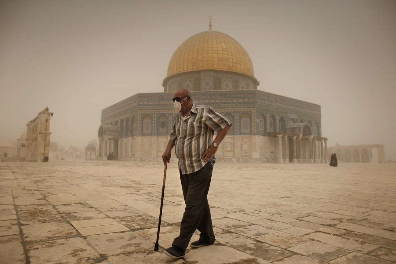 <p>A Palestinian man wears a mask to protect his face from the dust as he walks past the Dome of the Rock mosque in the al-Aqsa Mosque compound in Jerusalem, on Sept. 8, 2015.</p>