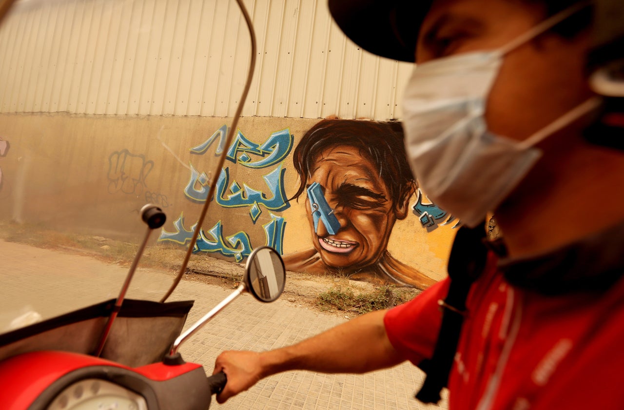 <p>A Lebanese man on his scooter wears a face mask as he drives past a graffiti painted wall during a sandstorm in Beirut on Sept. 8, 2015</p>