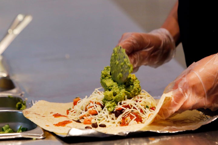 A Chipotle worker, who's presumably not sick, prepares a burrito.