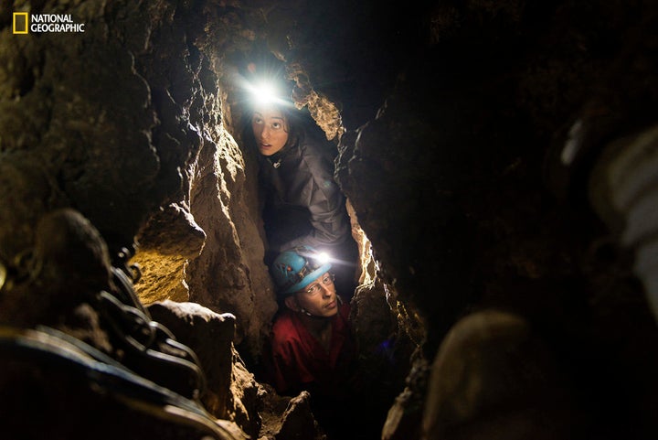 Lee Berger's daughter, Megan, acting as a safety caver on the expedition, and underground exploration team member Rick Hunter navigate the narrow chutes in the Rising Star cave in South Africa. 