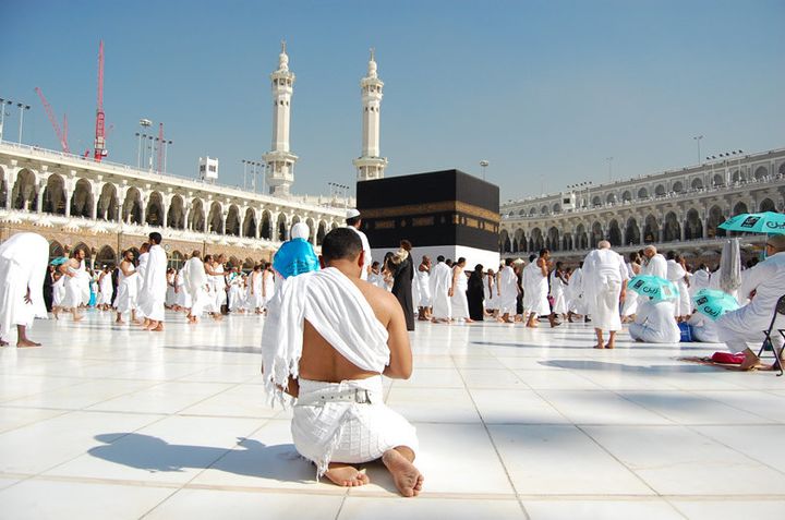 A pilgrim at the Kaaba in Mecca prays alone amongst a sea of the faithful. He sits in the traditional Islamic posture. 