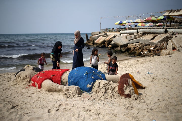 Palestinian girls put flowers on a sand sculpture on a Gaza City beach depicting Syrian refugee Aylan Kurdi, a 3-year-old boy who drowned offshore from Turkey.