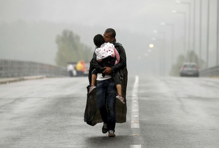 A Syrian refugee kisses his daughter as he walks through a rainstorm towards Greece's border with Macedonia, near the Greek village of Idomeni.
