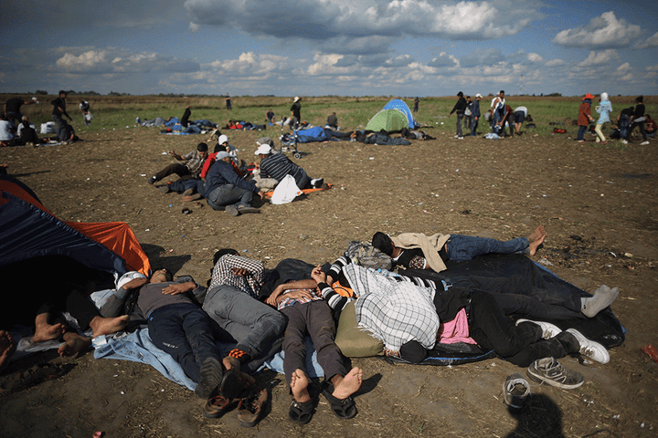 Exhausted migrants and refugees rest in a holding area after crossing the border from Serbia into Hungary near Roszke, on Sept. 6, 2015, and the same location on Sept. 16, 2015.