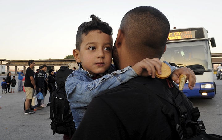 A Syrian refugee boy is carried toward a bus after disembarking a passenger ship at the port of Piraeus, near Athens, Greece,