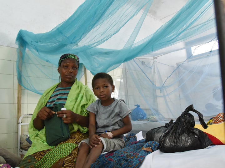 A mother sits with her sick child in a bed with mosquito net in a hospital on April 24, 2015 in the popular suburb of Port-Bo