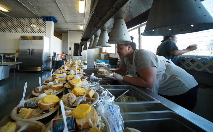 Staff ready plates for dinner consisting of a beef patty, rice, bread, cake and a slice of pineapple at the Institute of Human Services.