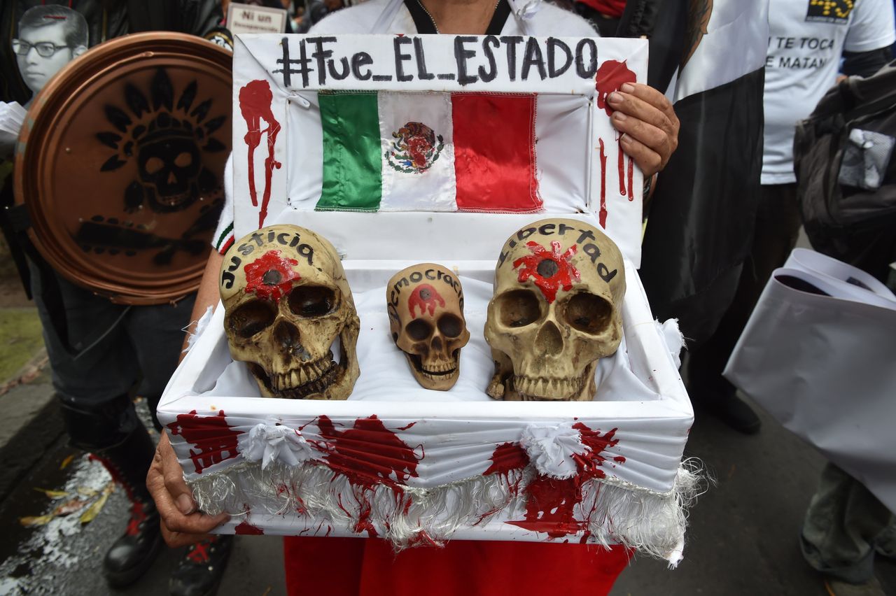 A woman holds a fake coffin with skulls marked justice, democracy and freedom, below a banner reading "It was the state" in Spanish.
