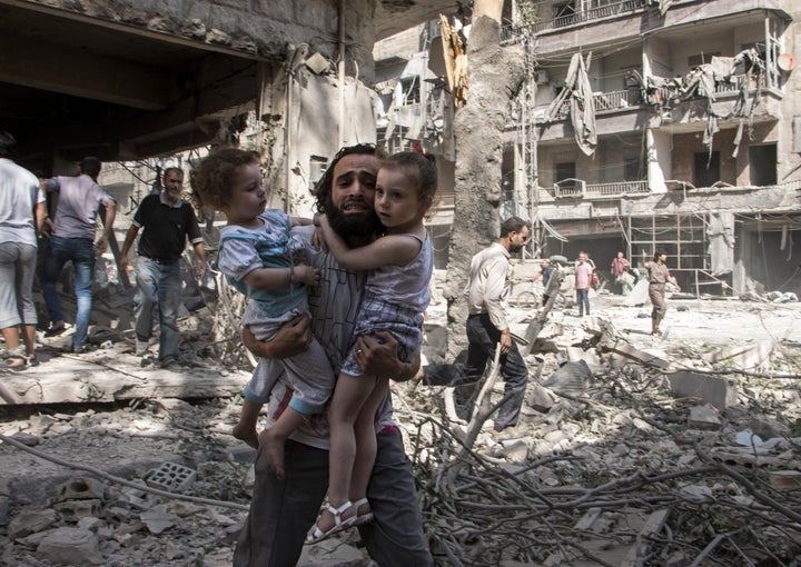 A Syrian man carries his two girls as he walks across the rubble following an airstrike in Aleppo on Sept. 17, 2015.