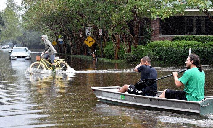 Two men row a boat as a cyclist passes nearby on a flooded street in downtown Charleston, South Carolina, on Oct. 4, 2015.