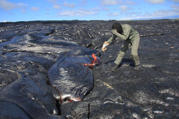 A Hawaiian Volcano Observatory scientist collects a molten lava sample using a rock hammer.