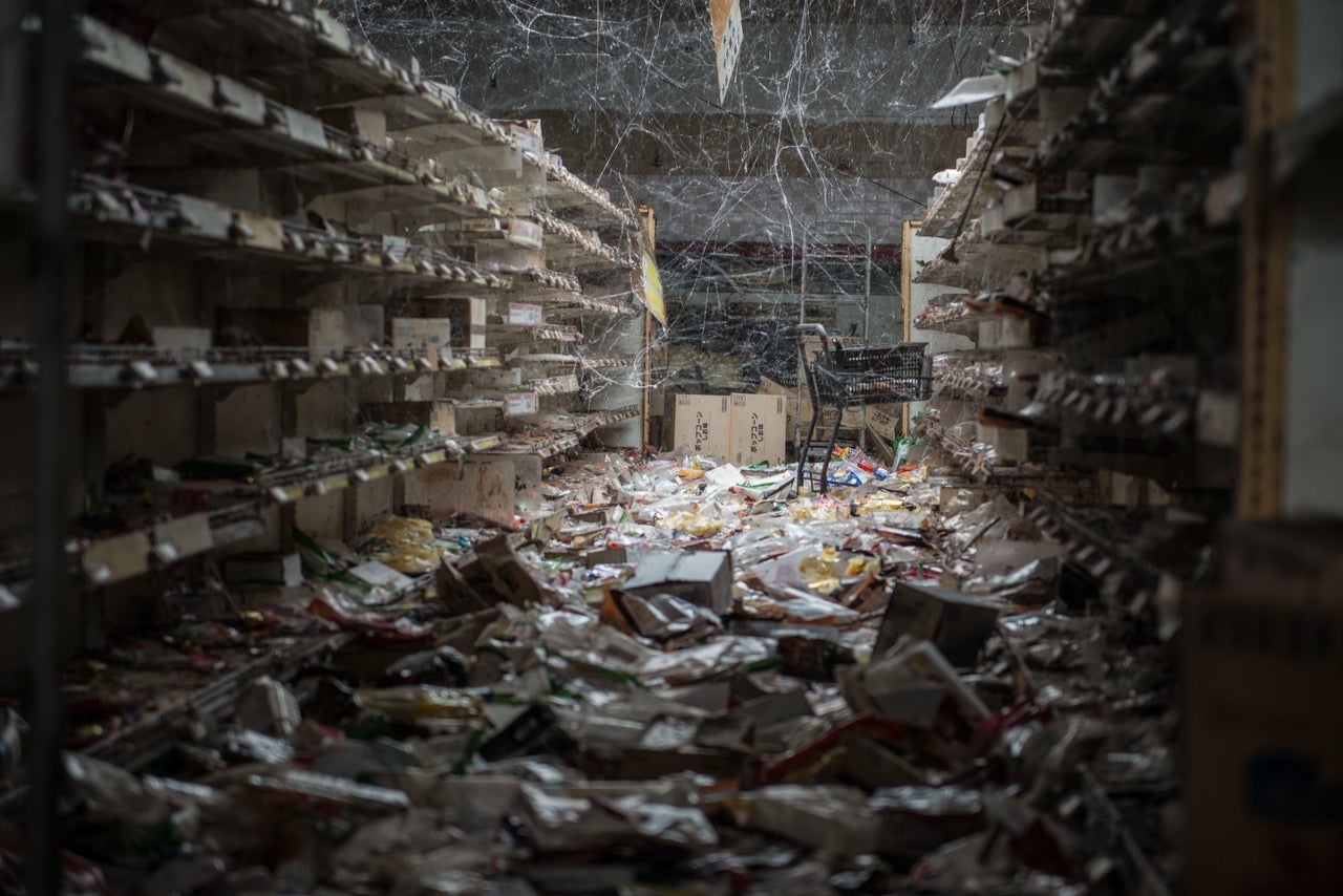 An aisle of a supermarket with products left on the floor. Since the disaster nature has been at work and cobwebs now hang between the shelves.