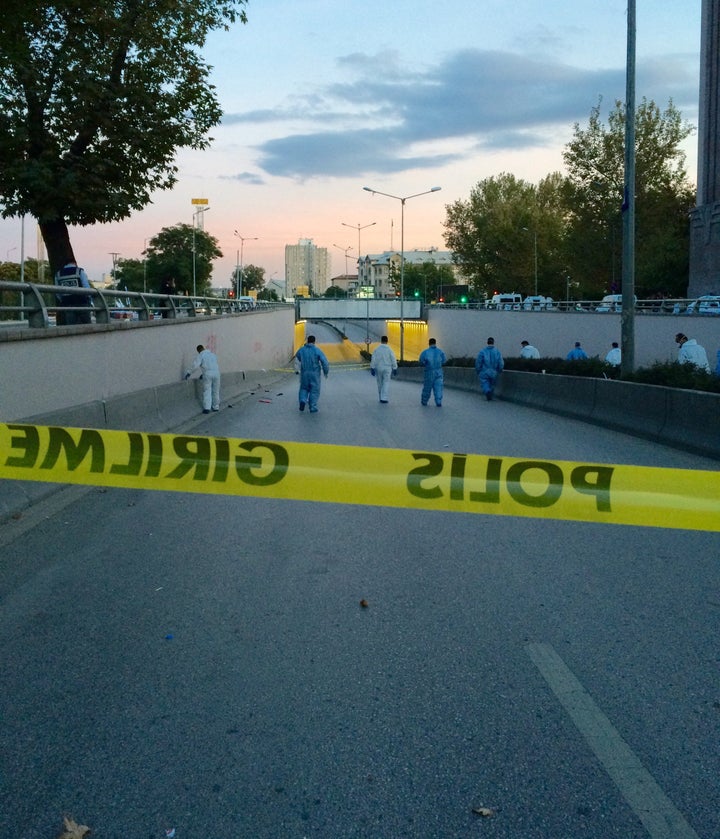 Men in full protective gear walk behind police tape, inspecting thebr         /damage after the morning's twin bombings. Police 