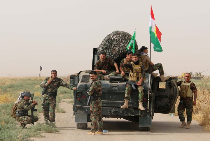 Iraqi Kurdish Peshmerga fighters pose for a photo next to a military vehicle bearing the Kurdish flag after they reportedly c